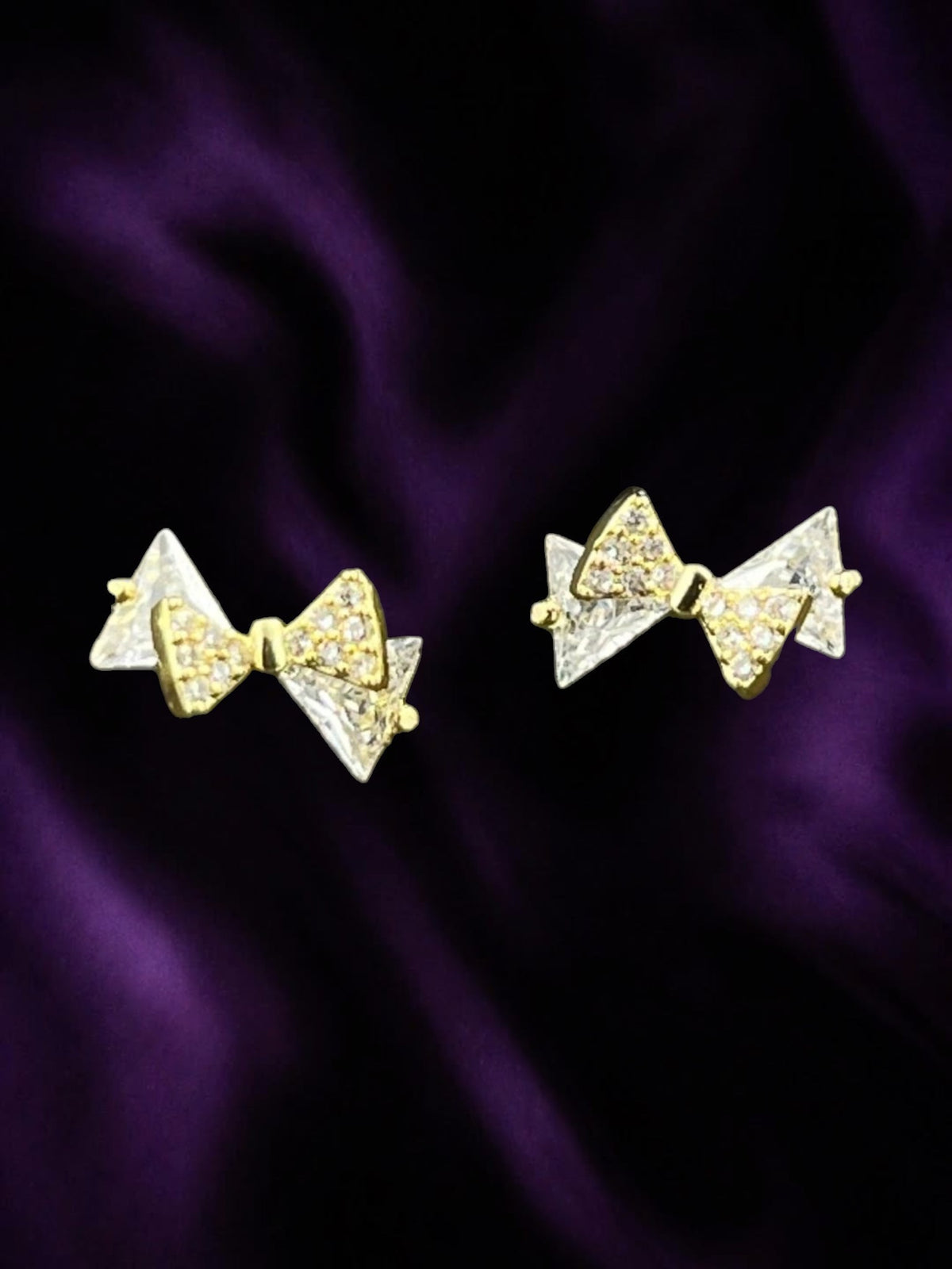 SHE BEAUTY DIAMOND RIBBON stud earrings featuring gold-tone bows with sparkling clear crystals on purple fabric