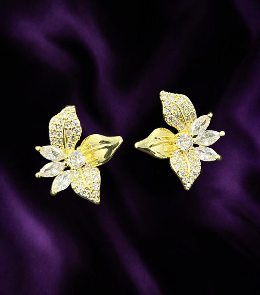 SHE BEAUTY S925 gold-tone flower stud earrings with sparkling cubic zirconia crystals on a dark purple satin background