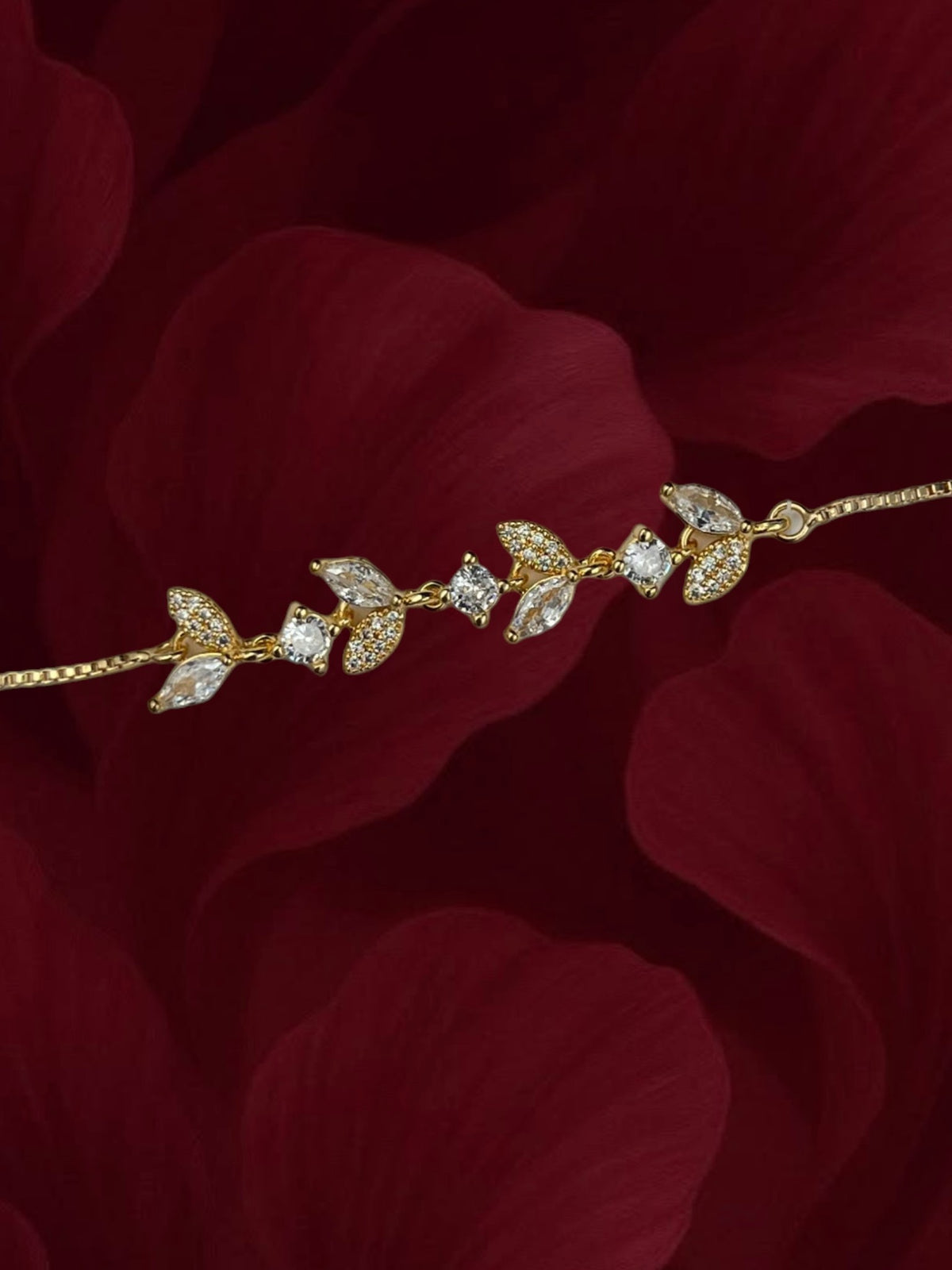 SHE BEAUTY gold-toned zirconia leaf bracelet with sparkling marquise and round stones on a dark red petal background