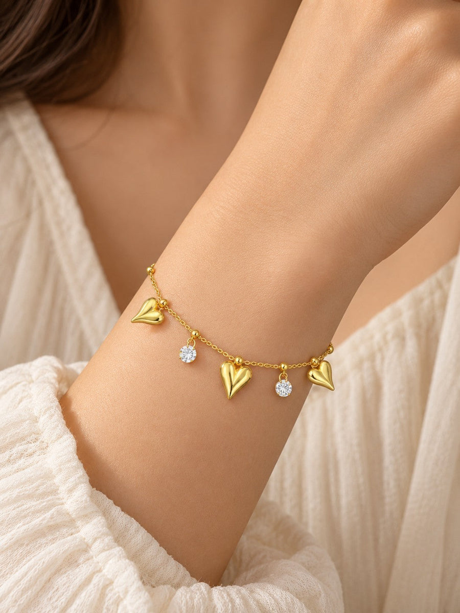 SHE BEAUTY gold chain bracelet featuring dangling heart charms and sparkling round crystals on a woman's wrist