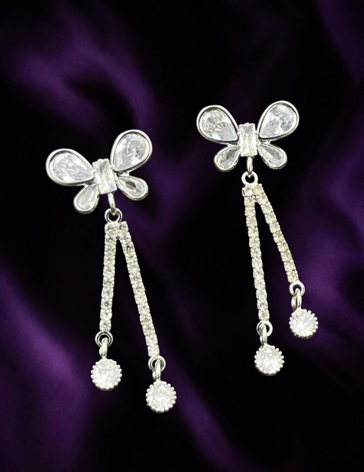 SHE BEAUTY AD butterfly earrings with sparkling cubic zirconia stones on a deep purple fabric background