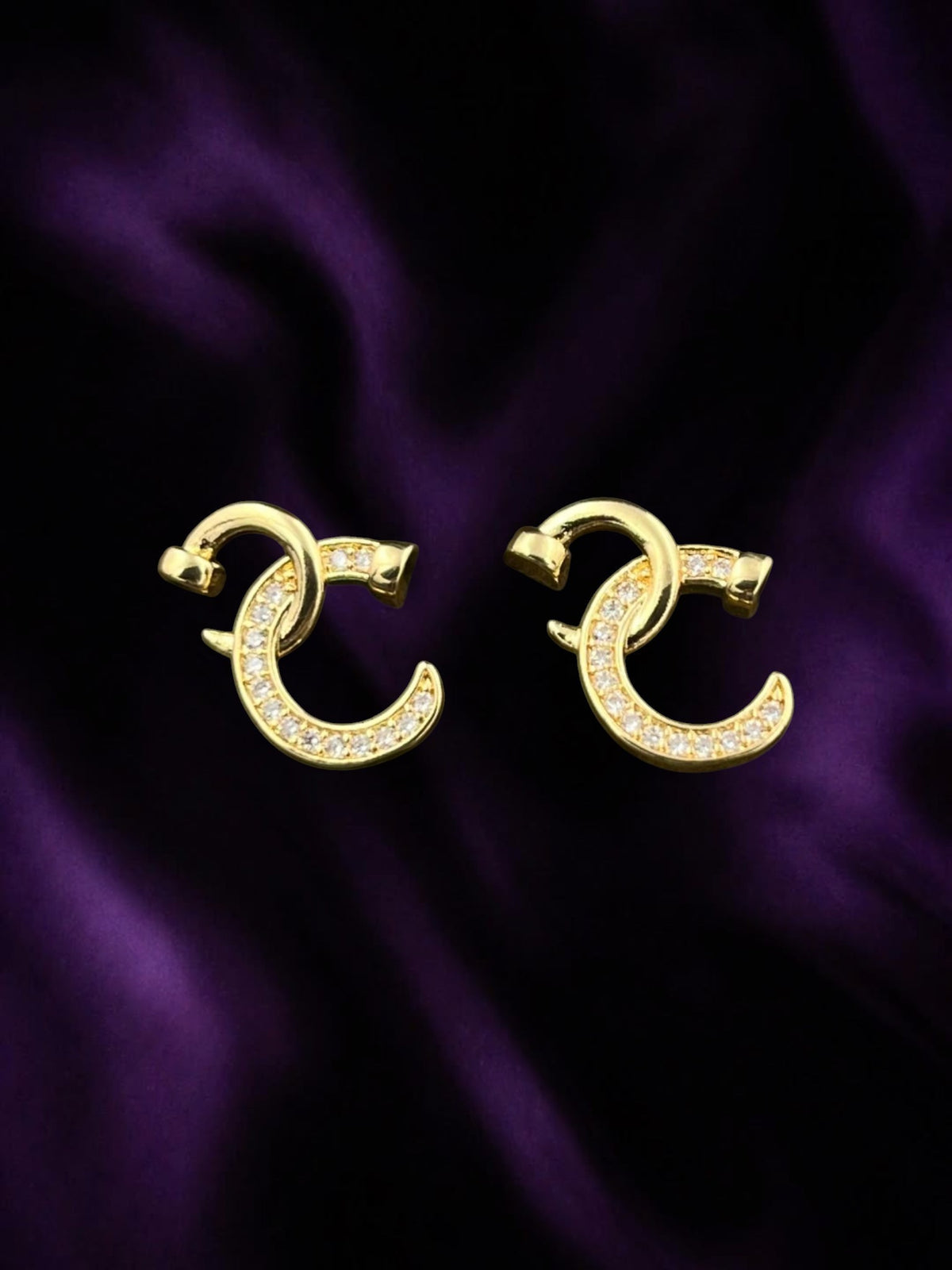 SHE BEAUTY CRYSTAL TWIST gold-toned earrings with a crescent shape and sparkling crystal accents on purple satin