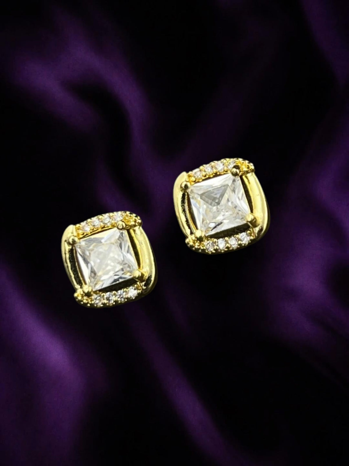 SHE BEAUTY DIAMOND EDGE square stud earrings with clear cubic zirconia stones set in gold-tone metal on purple silk