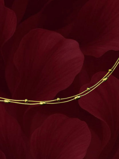 SHE BEAUTY KIYU ZIYU gold-toned double-strand anklet with delicate beads against a dark red floral background.