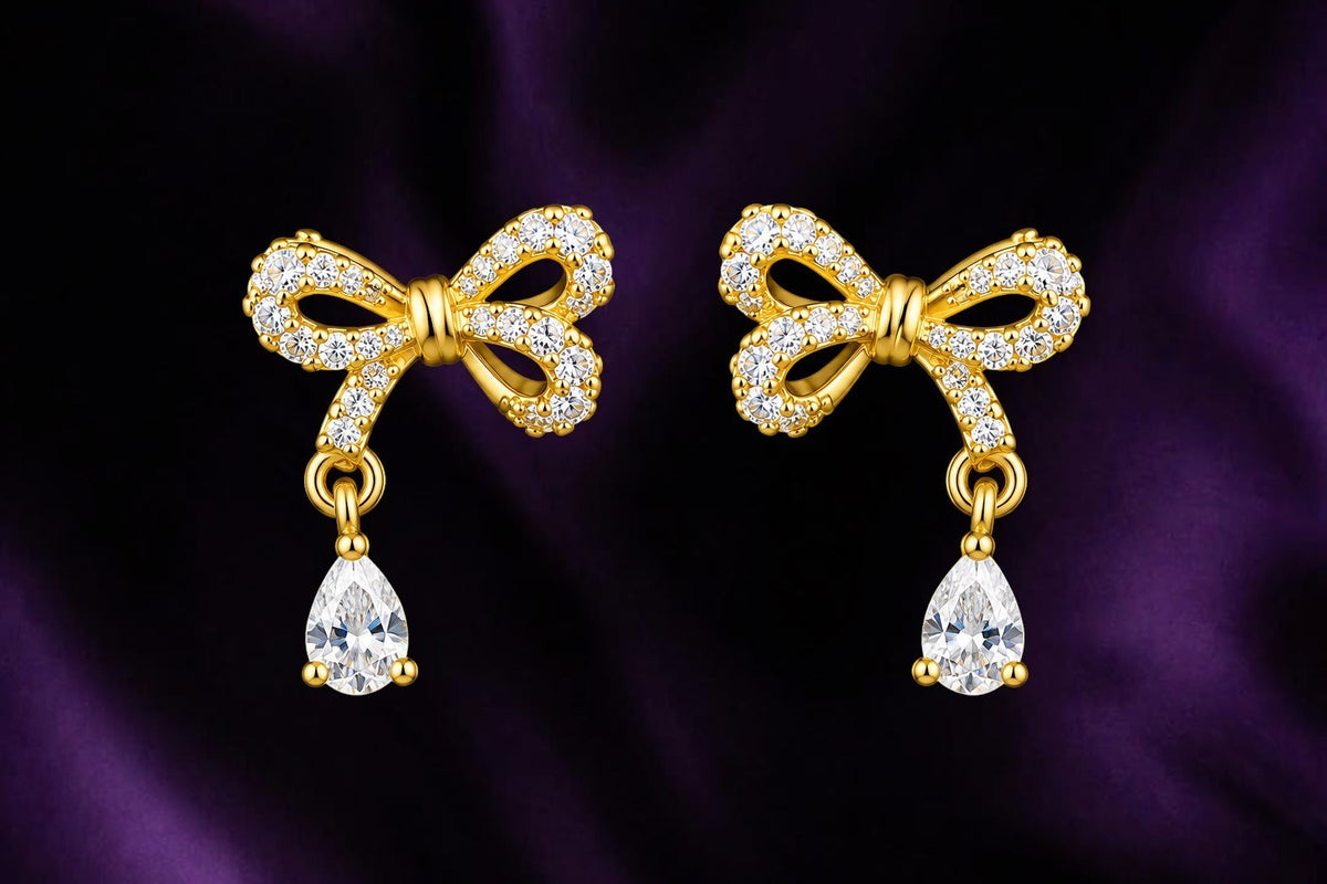 SHE BEAUTY GRACE BOW STUDS featuring gold-tone bows encrusted with clear crystals and dangling pear-cut stones.