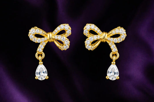 SHE BEAUTY GRACE BOW STUDS featuring gold-tone bows encrusted with clear crystals and dangling pear-cut stones.