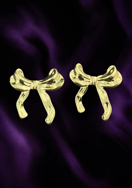 SHE BEAUTY anti-tarnish gold-toned bow-shaped stud earrings for festive and everyday wear on a purple satin background