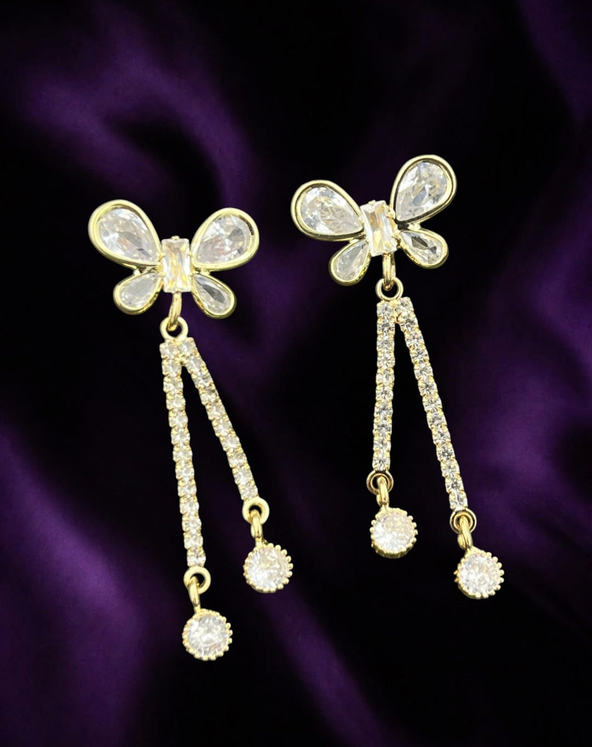 SHE BEAUTY gold-tone butterfly earrings featuring sparkling AD stones and dangling crystal accents on purple satin