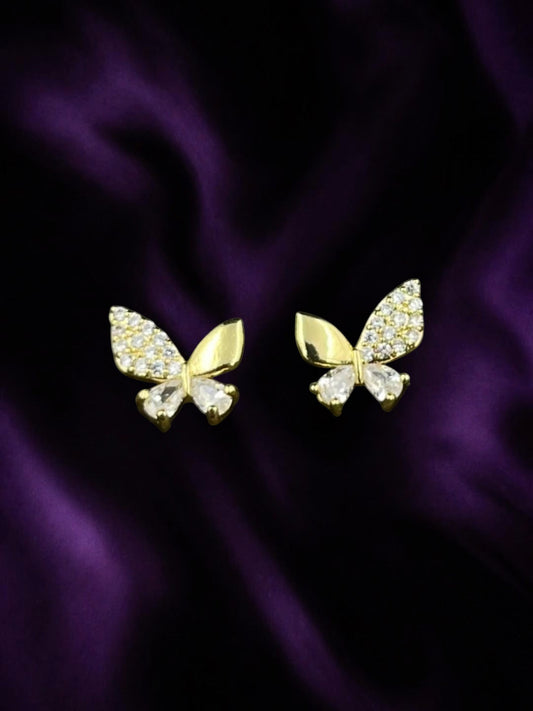 SHE BEAUTY BUTTERFLY GLOW gold butterfly stud earrings with sparkling crystal accents on a purple satin background