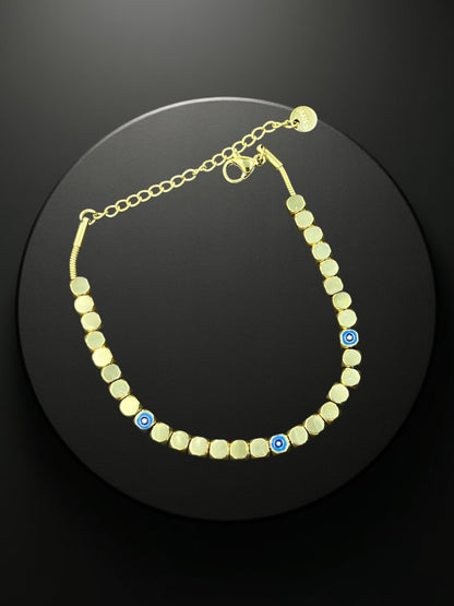SHE BEAUTY KIYU ZIYU gold-tone chain bracelet featuring square beads and blue evil eye charms on a black display.