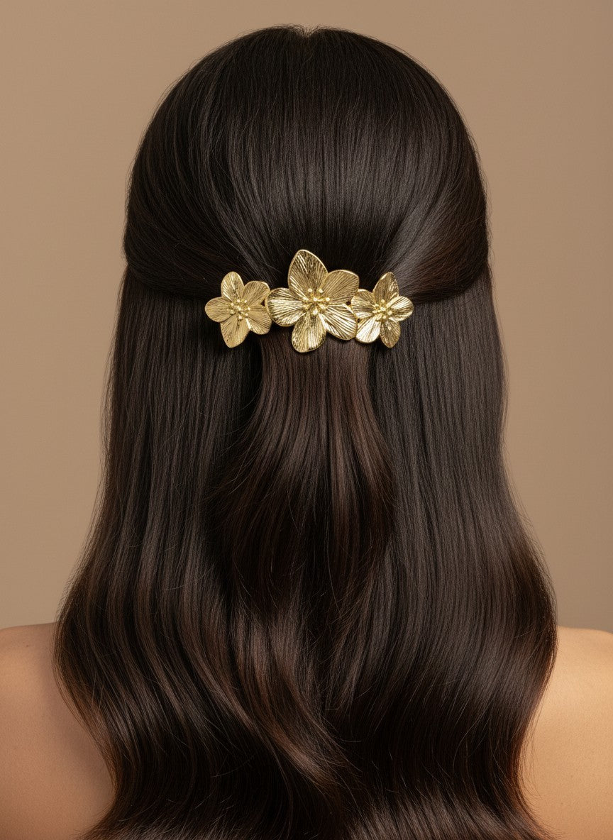 SHE BEAUTY gold metallic blossom barrette worn in dark hair for a festive floral hair accessory look