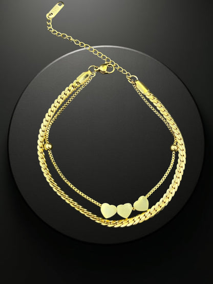 SHE BEAUTY KIYU ZIYU gold-toned double-layer chain bracelet featuring three heart charms on a black display stand.
