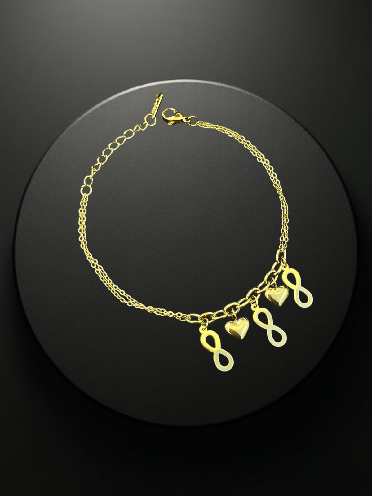 SHE BEAUTY KIYU ZIYU gold-tone chain bracelet featuring infinity and heart charms on a black circular display base.