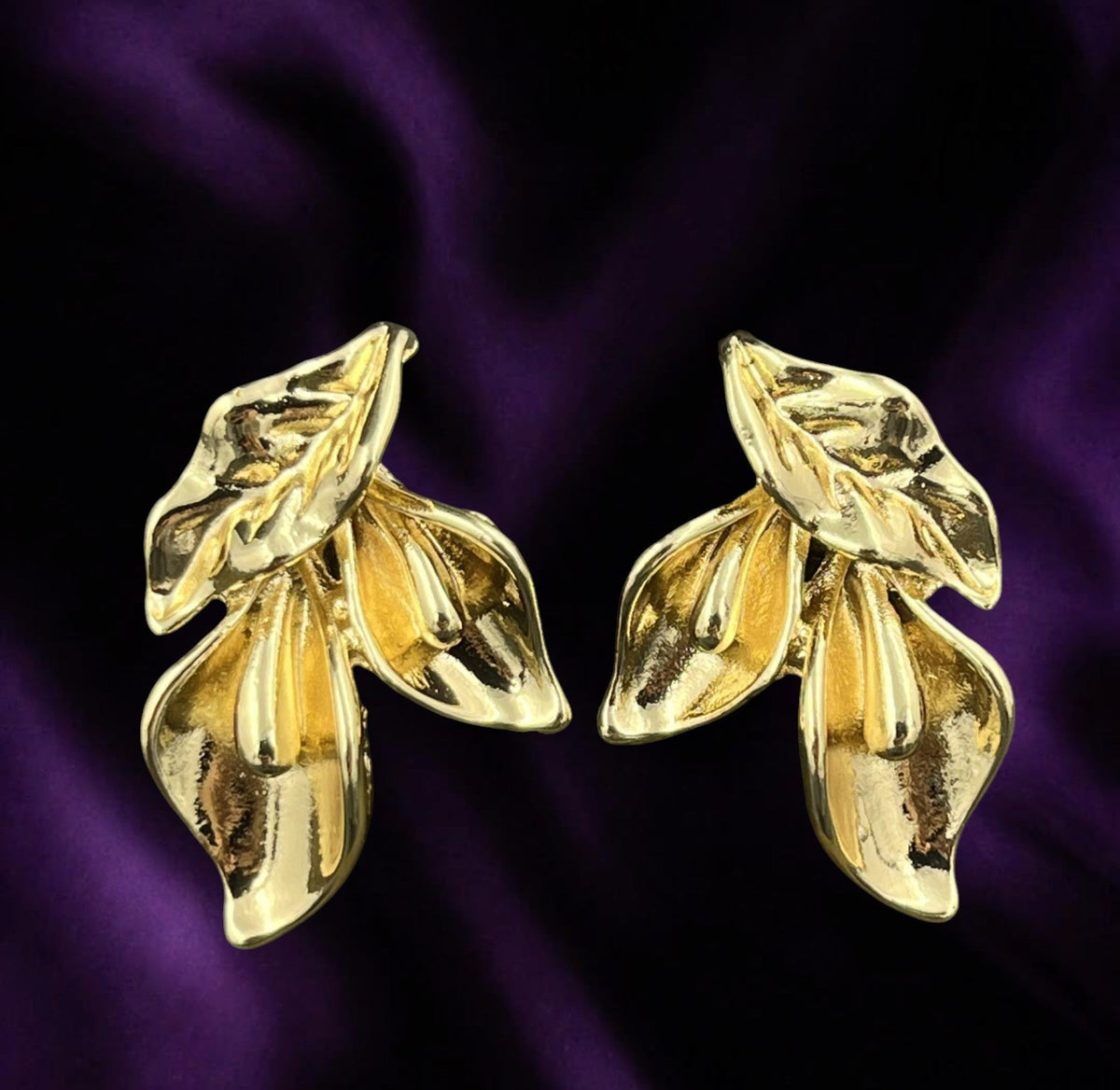 SHE BEAUTY gold-toned anti-tarnish earrings featuring a stylish floral leaf design on a deep purple fabric background.