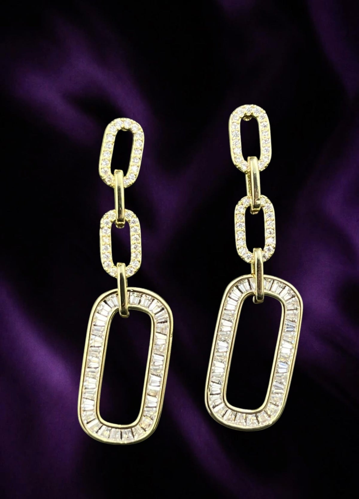 SHE BEAUTY gold-toned link drop earrings featuring baguette and round cubic zirconia stones on a purple fabric