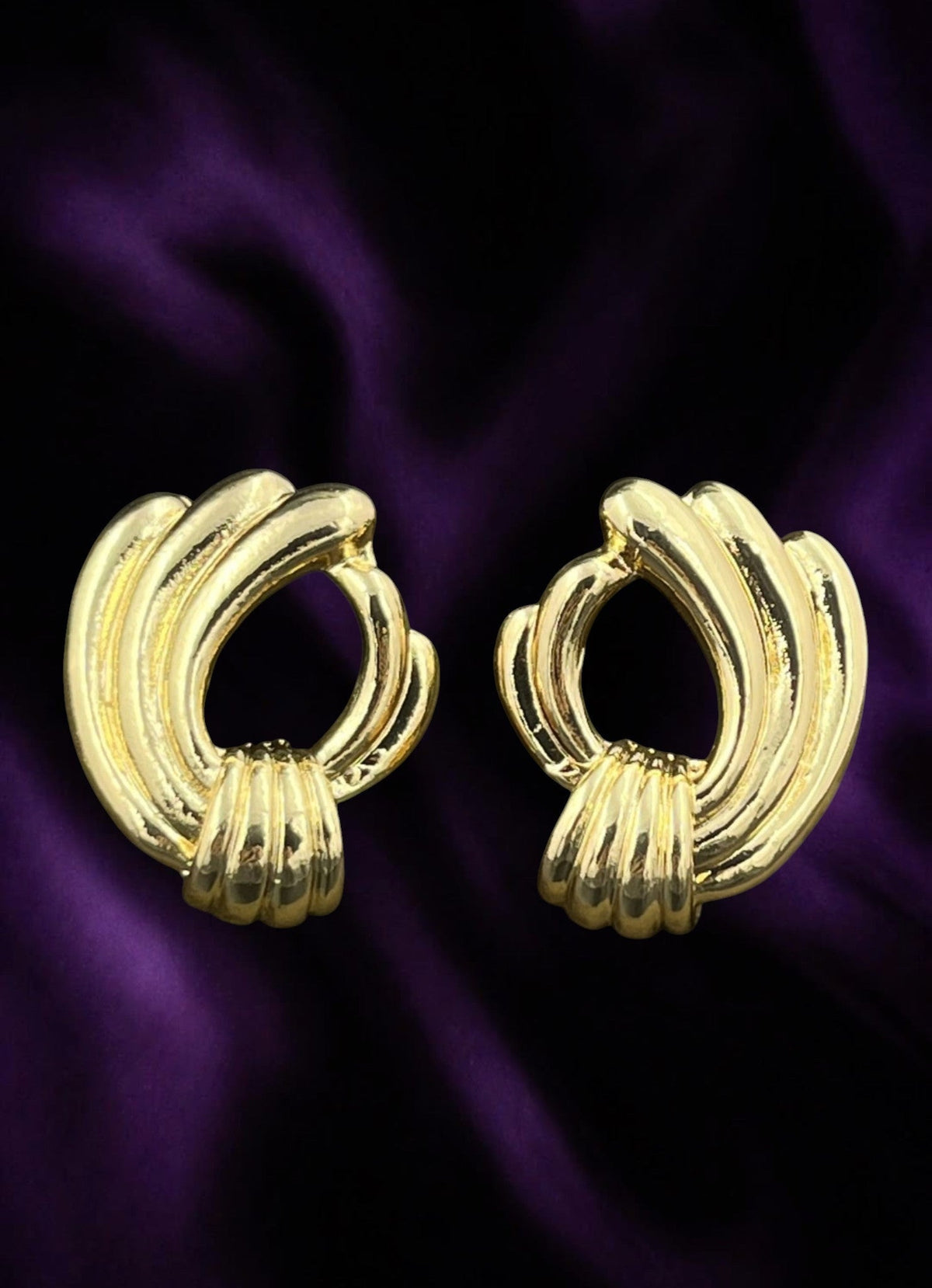 SHE BEAUTY anti-tarnish gold-toned statement earrings with a polished ribbed design on a dark purple satin background.