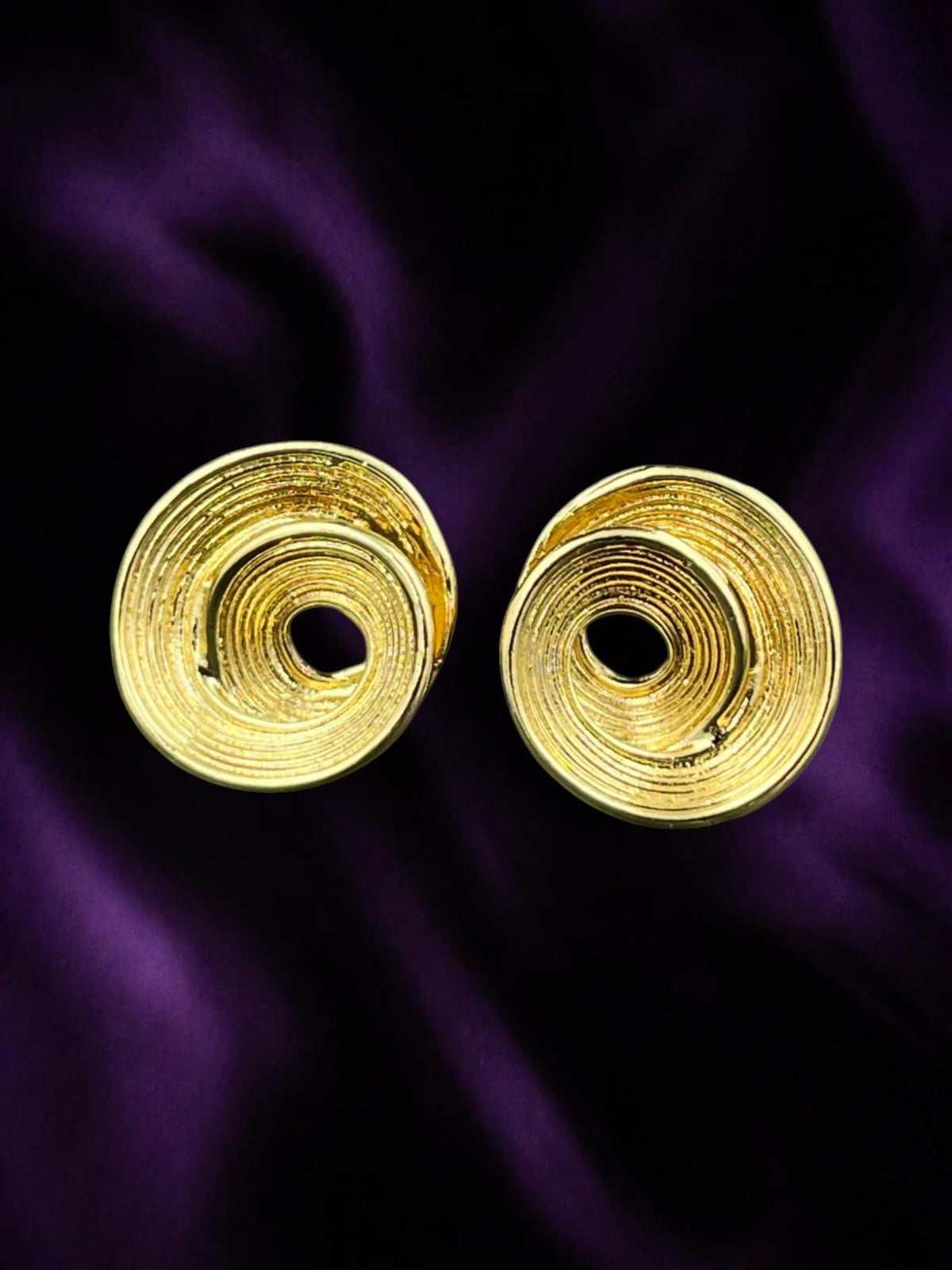 SHE BEAUTY anti-tarnish gold-toned spiral stud earrings with a textured finish on a deep purple satin background.