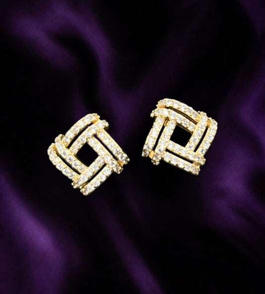 SHE BEAUTY gold-toned square stud earrings with sparkling cubic zirconia stones on a dark purple satin background