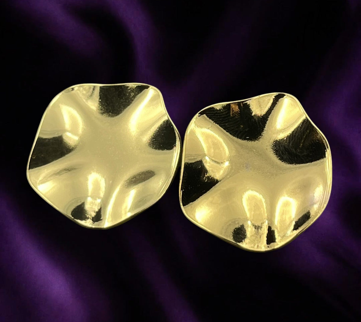 SHE BEAUTY anti-tarnish gold-toned statement earrings with a wavy, organic shape on a purple satin background.