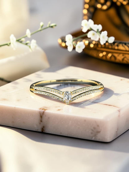 SHE BEAUTY gold anti-tarnish bracelet featuring a V-shaped design with sparkling zirconia stones on a marble stand.