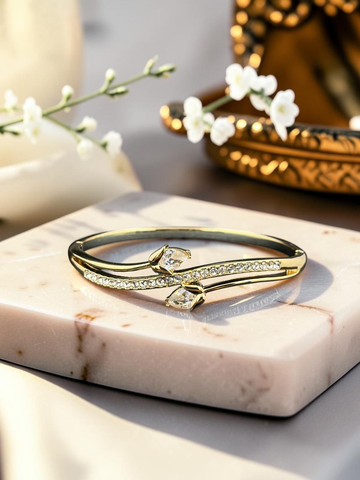 SHE BEAUTY gold anti-tarnish bracelet featuring a bypass design with sparkling zirconia stones on a marble display