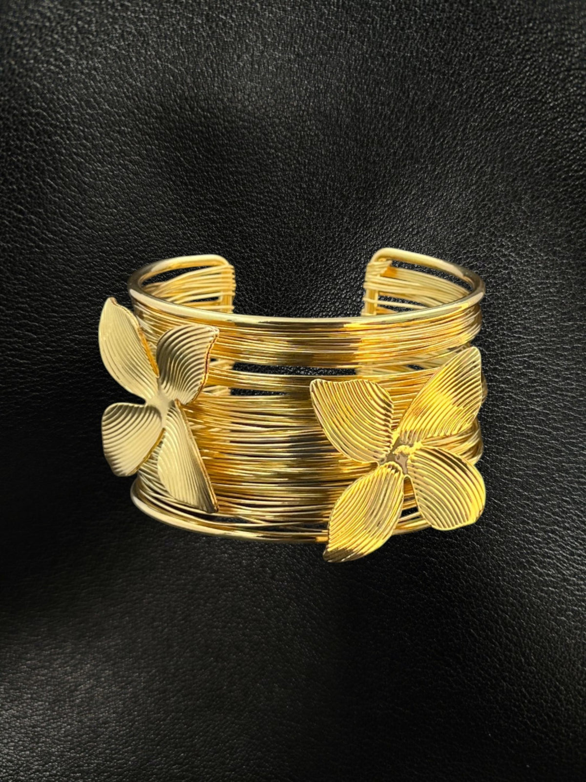 SHE BEAUTY golden multilayer cuff bracelet featuring delicate metallic flower accents on a black leather background.