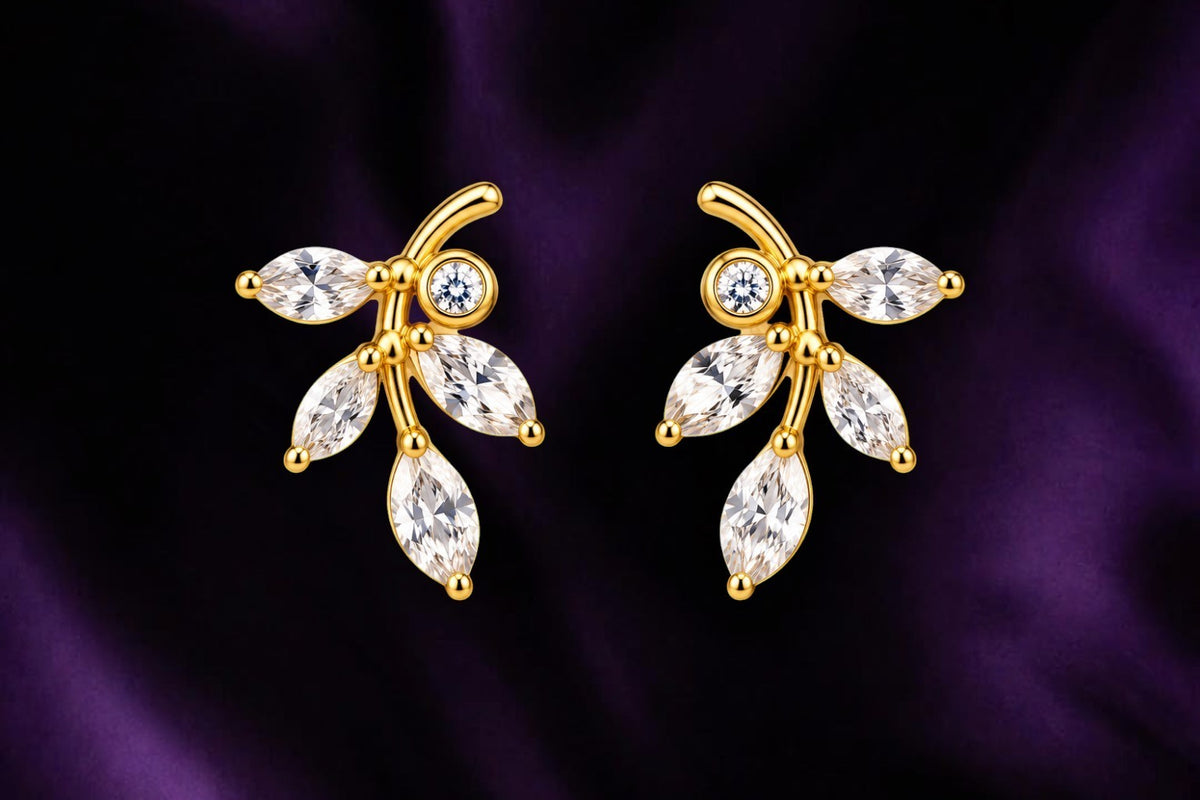 SHE BEAUTY golden vine stud earrings featuring marquise-cut crystals and a round stone on a dark purple silk background
