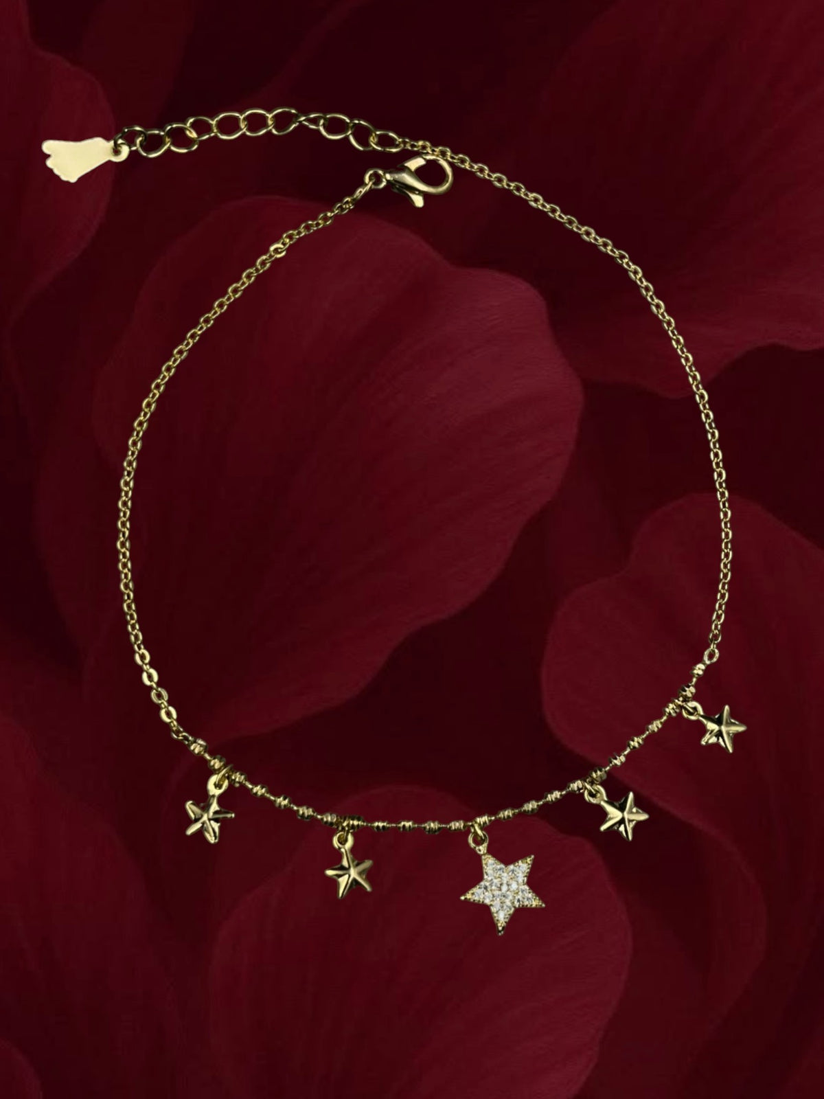 SHE BEAUTY kids anti-tarnish gold-tone anklet featuring dangling star charms on a delicate chain against red petals
