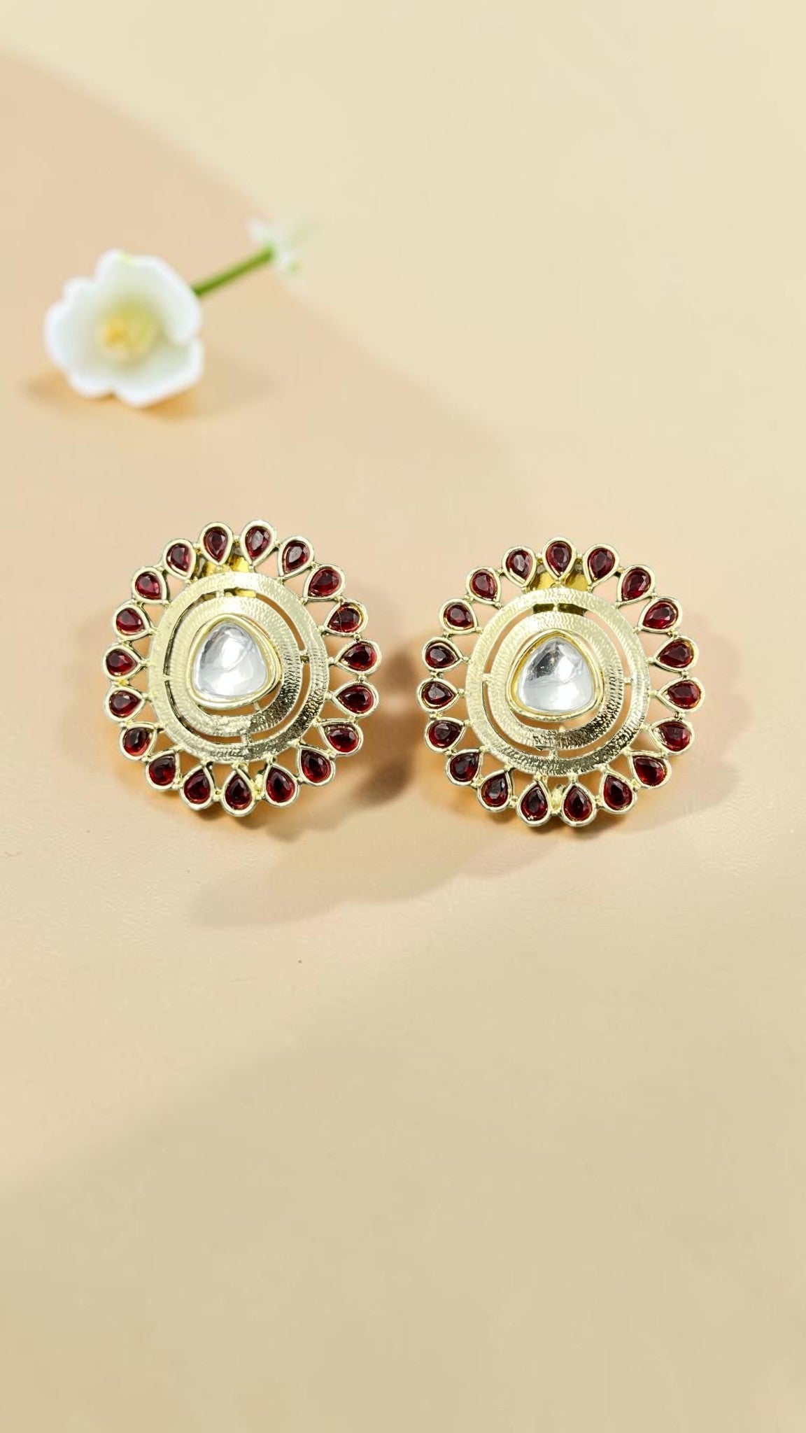 SHE BEAUTY round kundan tops featuring a central clear stone surrounded by red teardrop accents in a gold finish