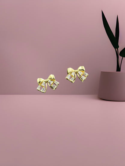 SHE BEAUTY LUXE BOW gold-toned earrings featuring sparkling baguette-cut crystals in a delicate ribbon design.