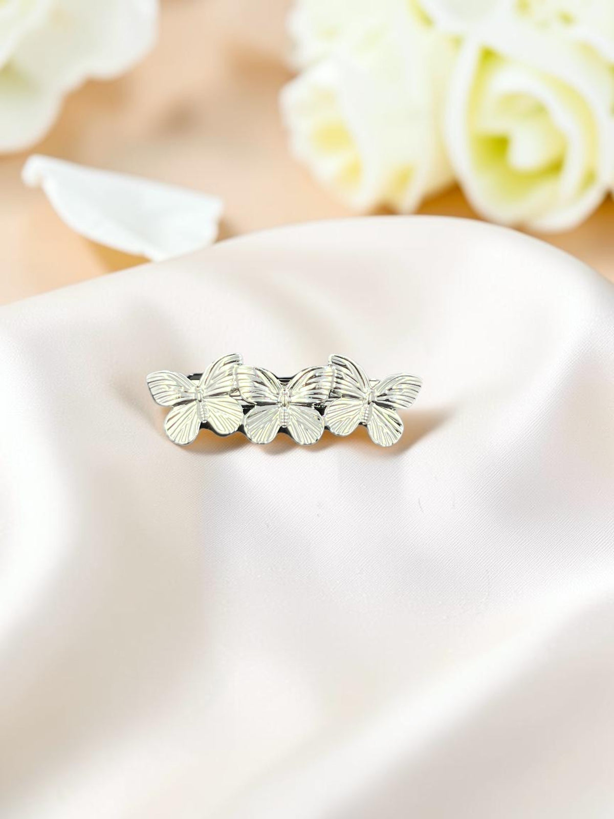 SHE BEAUTY metallic butterfly barrette featuring three silver-toned butterflies on a soft satin fabric background.