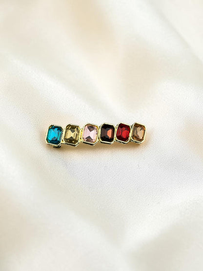 SHE BEAUTY barrette featuring six rectangular multi-colored gemstones in a gold-tone setting on cream fabric.