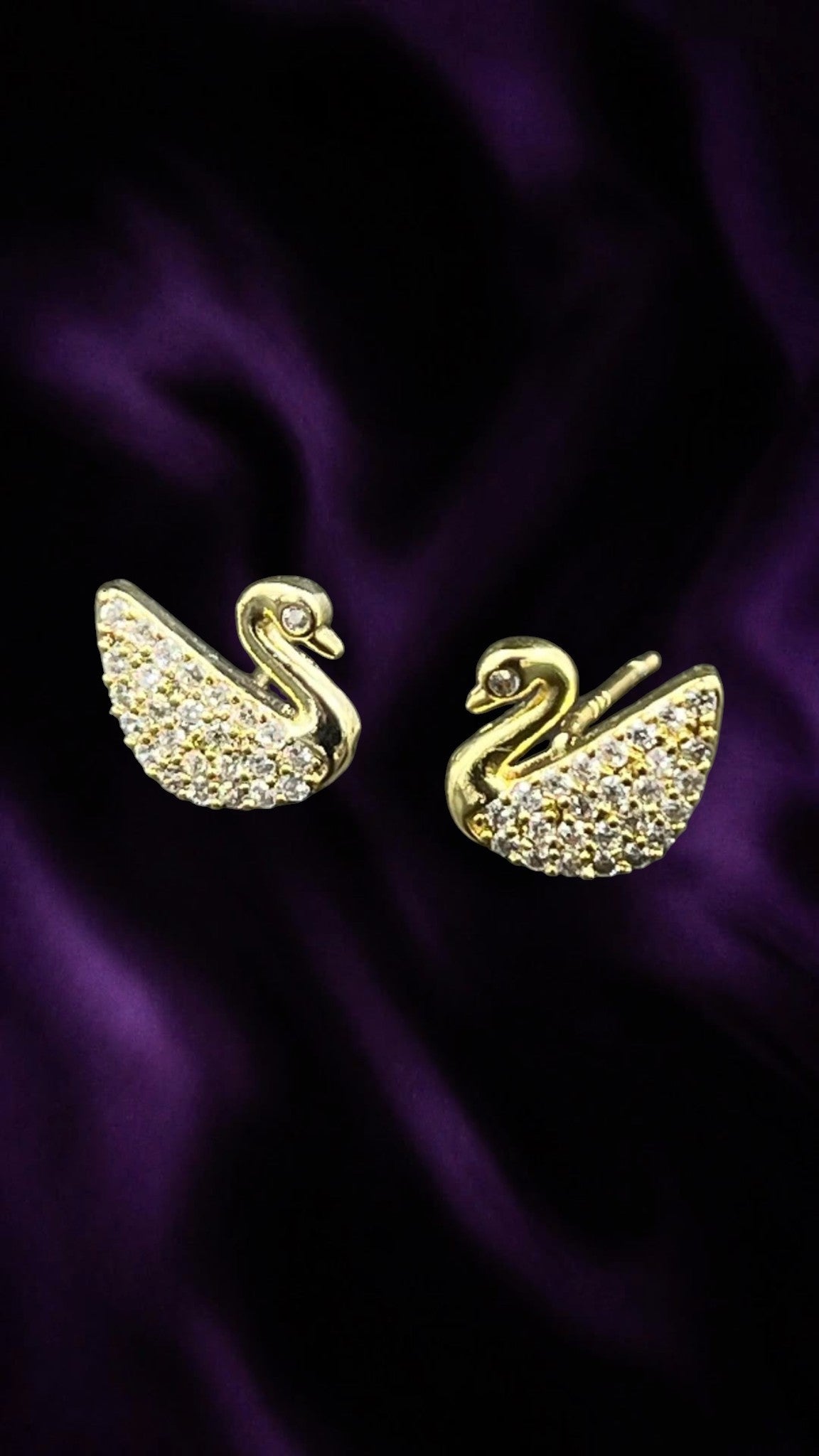 SHE BEAUTY SWAN GRACE gold-toned swan stud earrings featuring sparkling crystal embellishments on a purple background