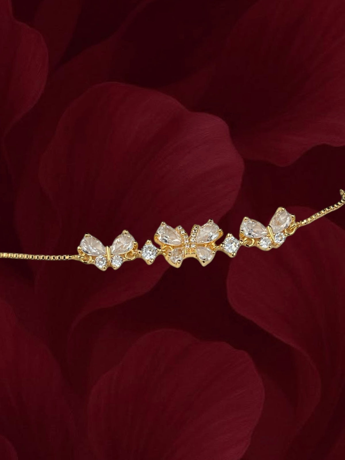 SHE BEAUTY gold-toned bracelet featuring delicate zirconia butterfly wings on a fine chain against a red floral backdrop