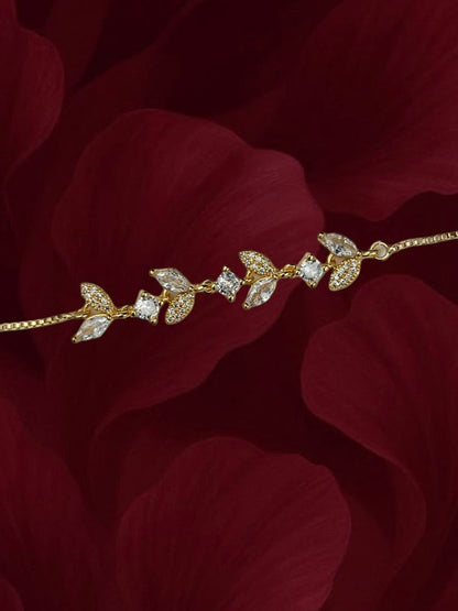 SHE BEAUTY gold-toned zirconia leaf bracelet with sparkling marquise and round stones on a dark red petal background
